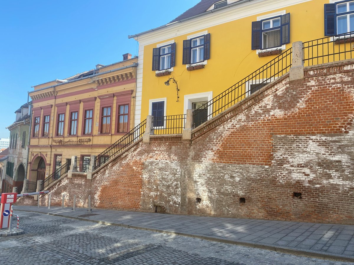 A yellow building with blue shutters above an old brick stairway and cobbled street in Sibiu
