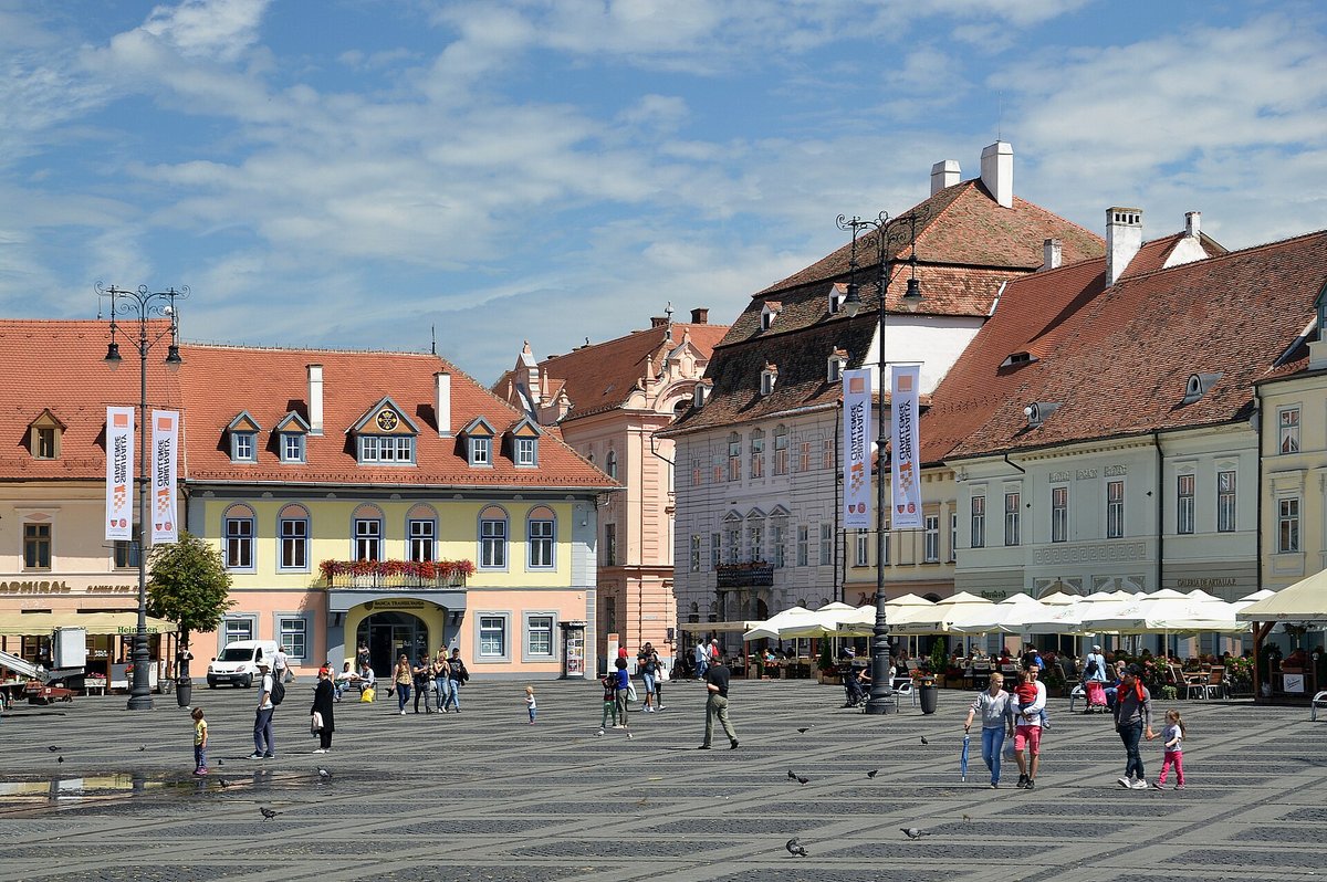 Piața Mare in Sibiu, a wide square lined with pastel historic buildings, red roofs and outdoor café umbrellas
