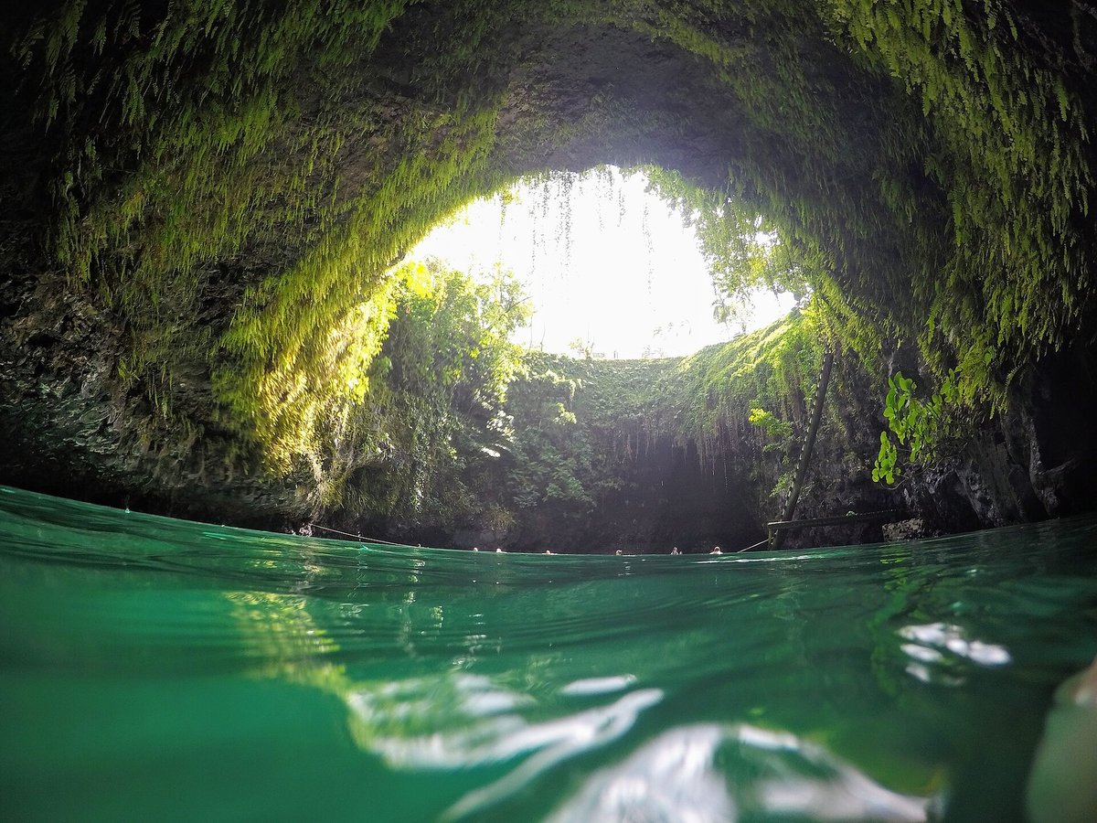 Looking up from a cave at the sunlit opening of To Sua Ocean Trench above green water
