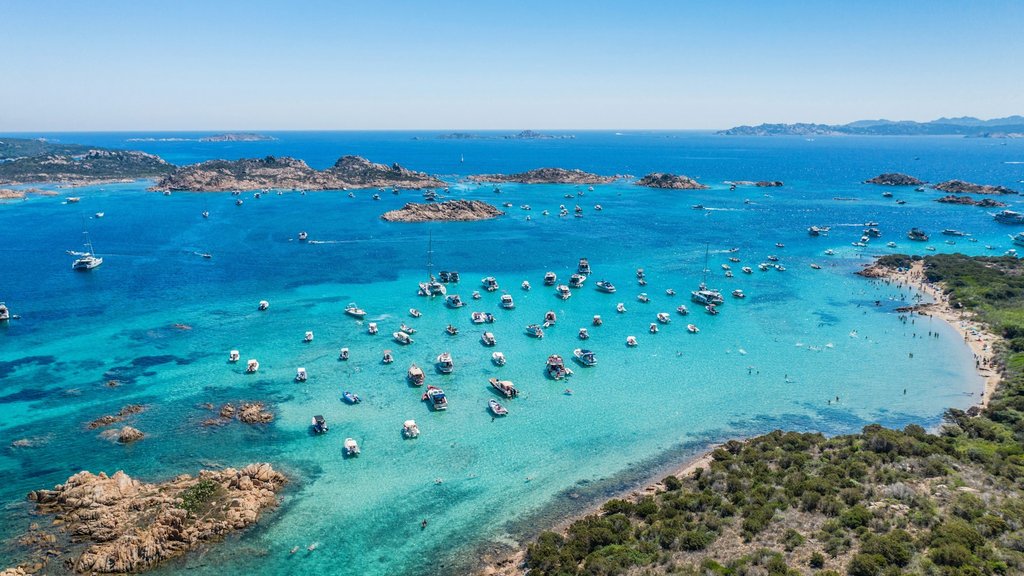 イタリア・サルデーニャのターコイズブルーの入り江の空撮。澄んだ地中海、岩の小島、沖に停泊する船、緑の植生に縁取られた砂浜