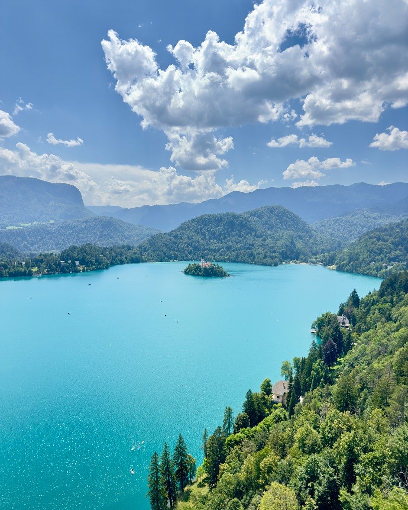Lake Bled from above, with the island church, forested hills and turquoise water under a summer sky
