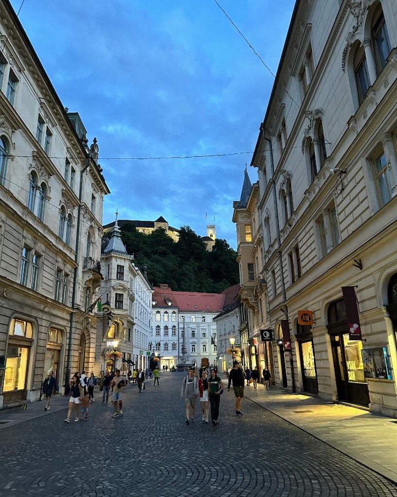 Ljubljana old town at dusk, with cobbled street, shopfronts and the castle on the hill