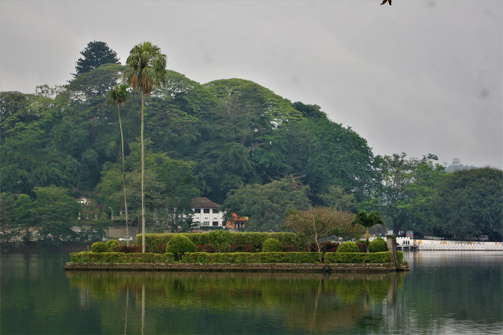 Small island house and calm water on Kandy Lake with green hills beyond