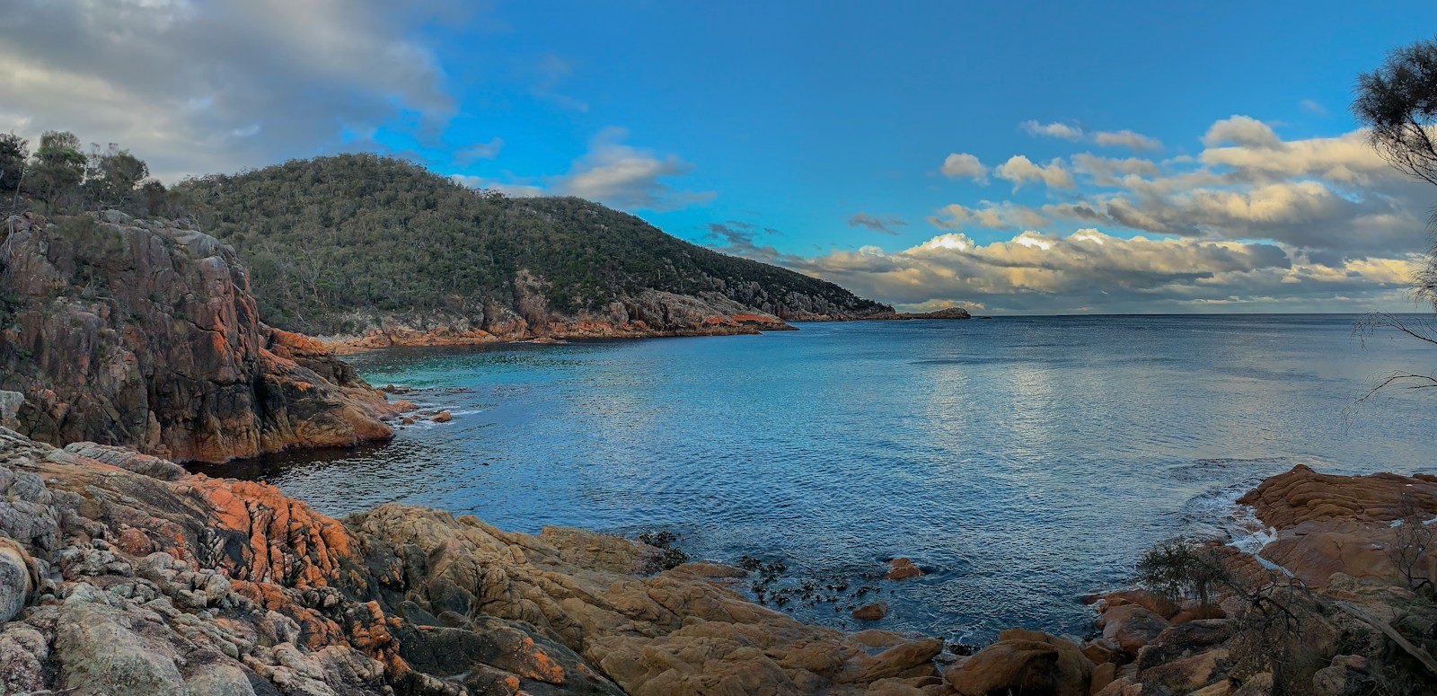 Rocky coastline at Freycinet with forested hills beneath a dramatic sky