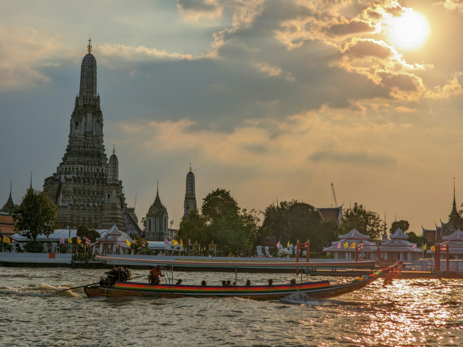 A boat sails past Wat Arun on the Chao Phraya River at sunset