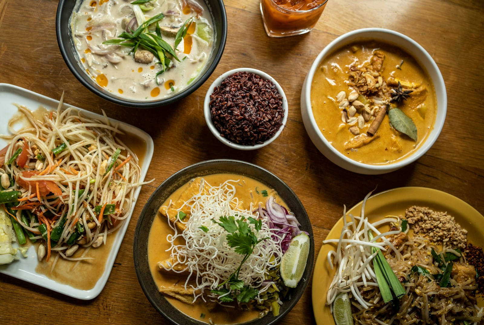 Wooden table topped with plates of Thai food