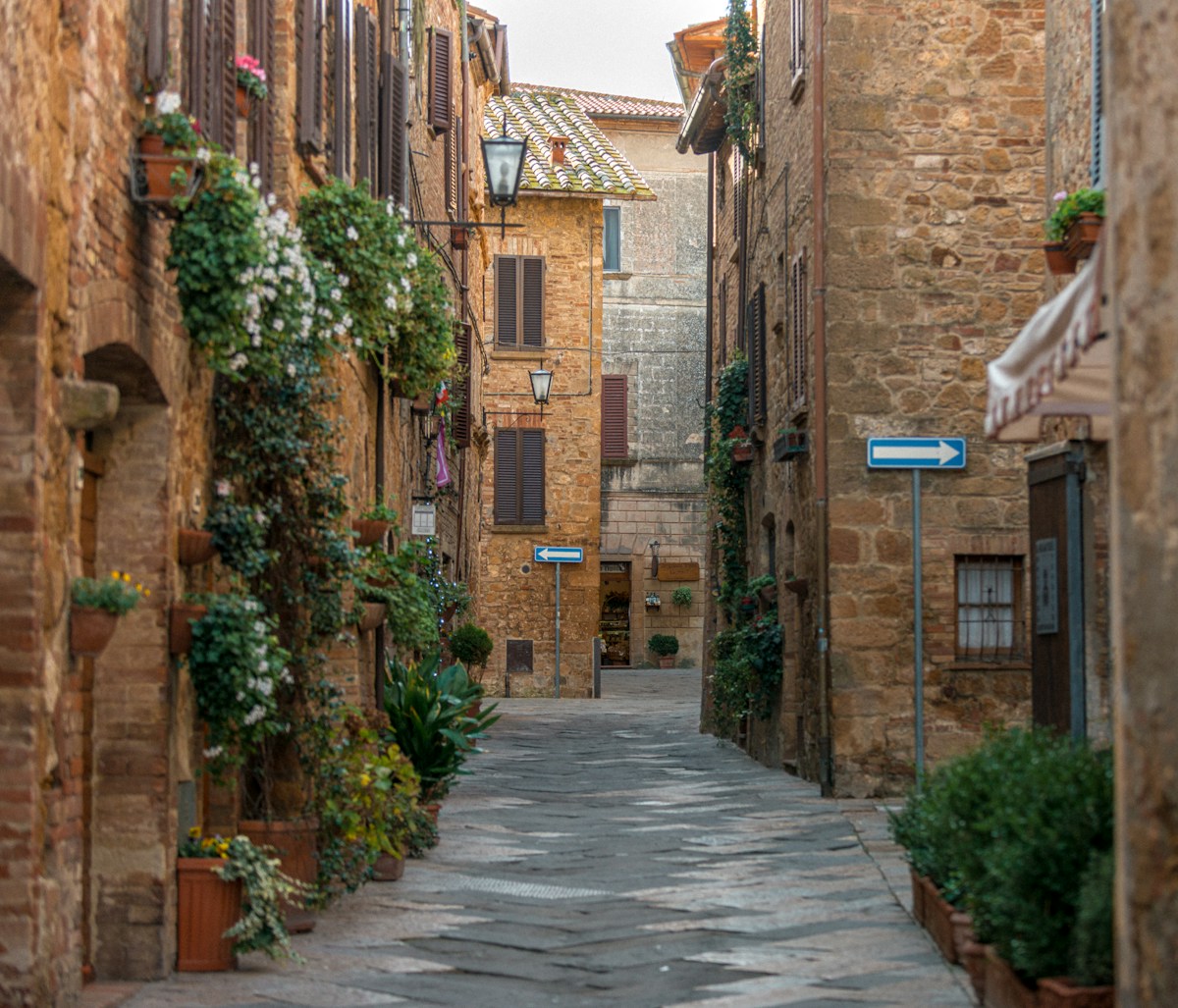 Narrow plant-lined stone alley in a historic Tuscan hill town near Pienza