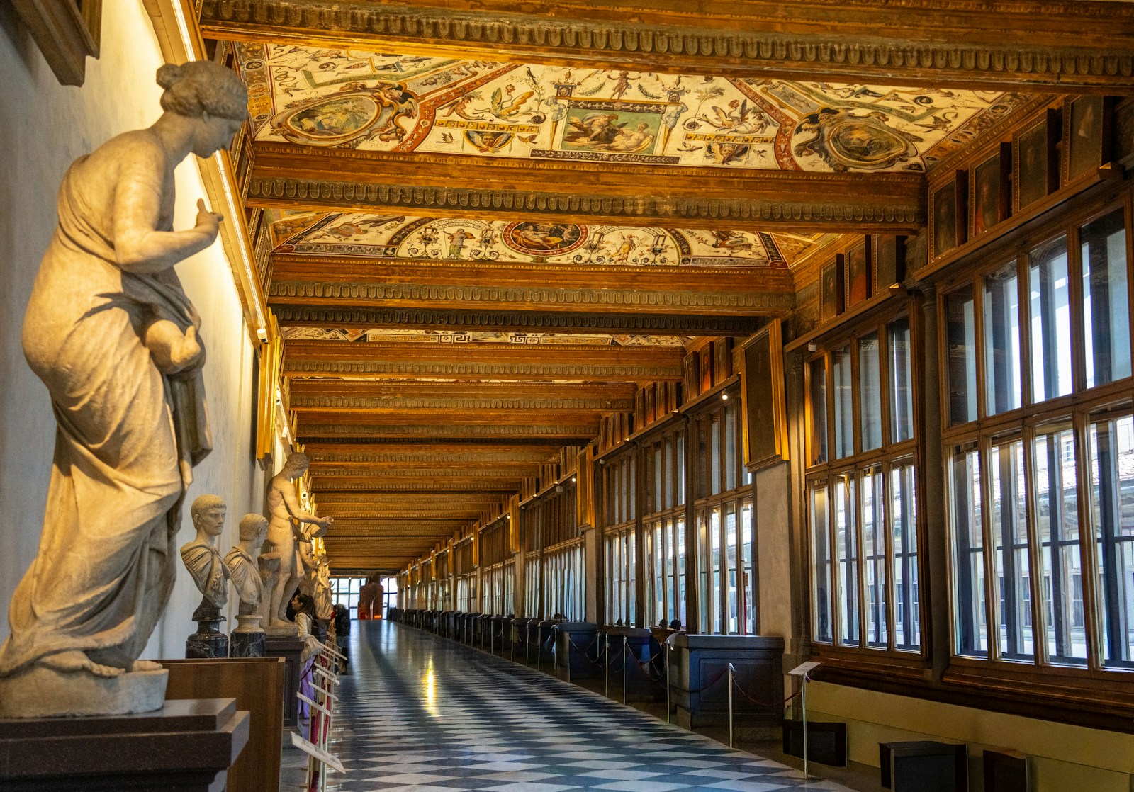 Long gallery hallway in the Uffizi with classical statues, frescoed ceiling and checkered marble floor