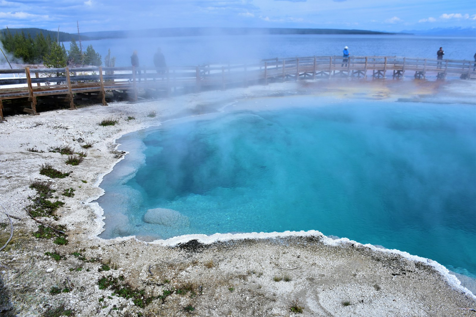 Steaming turquoise hot spring and boardwalks at West Thumb Geyser Basin beside Yellowstone Lake